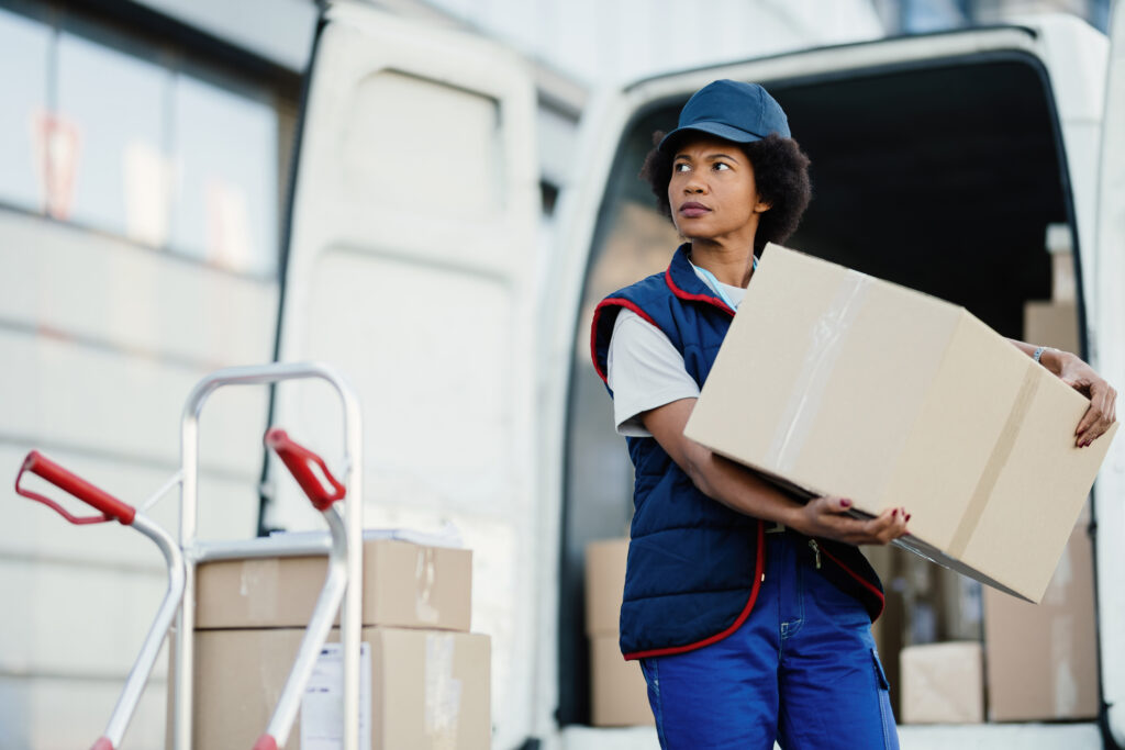 Black Female Courier Unloading Cardboard Boxes From Van While Making Delivery City 1024x683